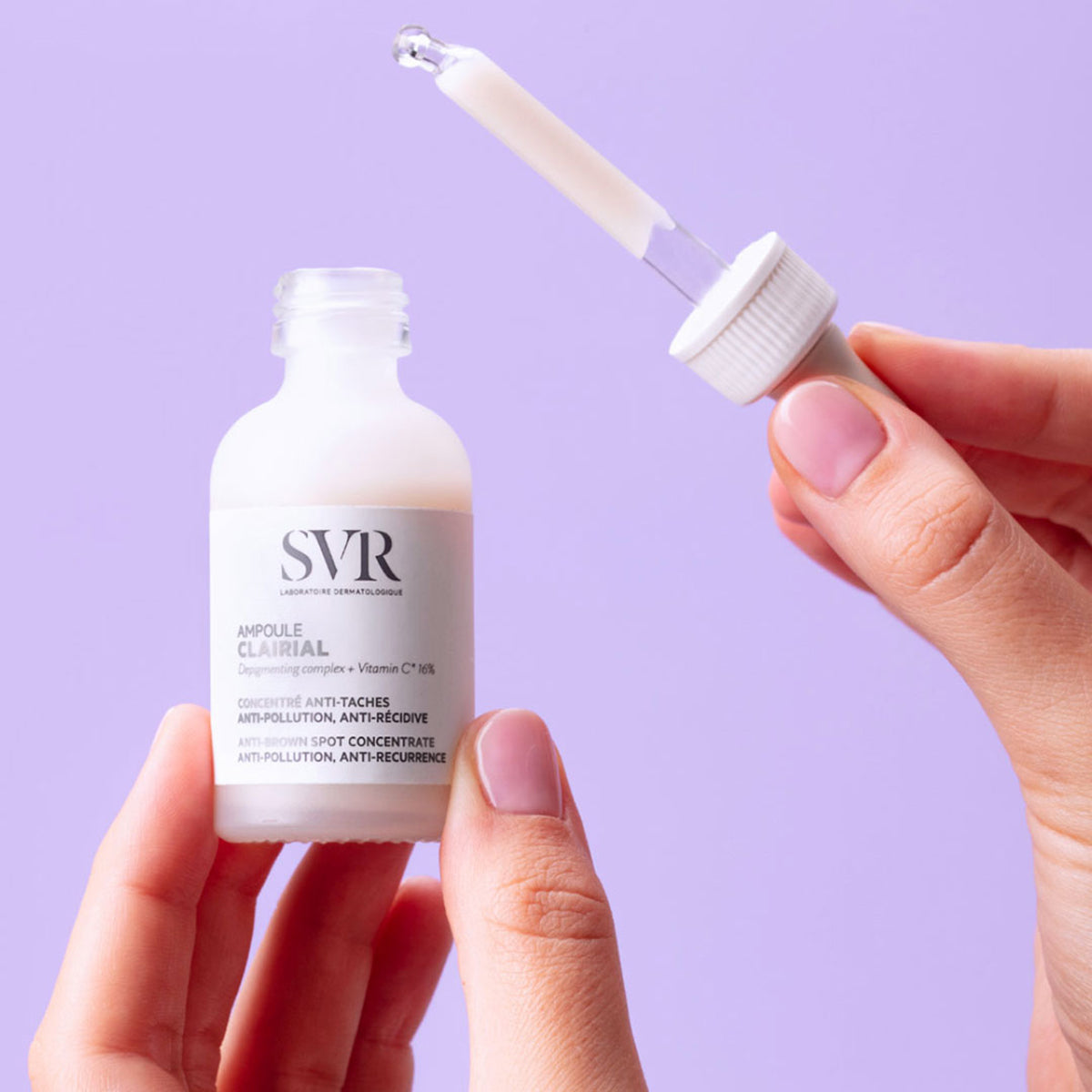 SVR Clairial Ampoule într-o sticlă de sticlă mată cu pipetă, ținută în mâini pe un fundal mov deschis.