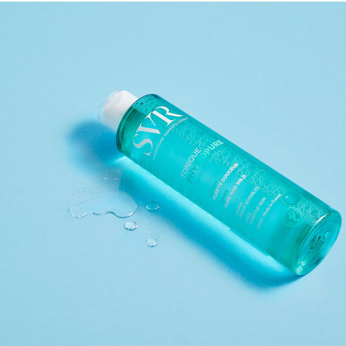 Flacon transparent de 200ml cu loțiune tonică albastră SVR PHYSIOPURE, așezat pe un fundal albastru cu picături de lichid.