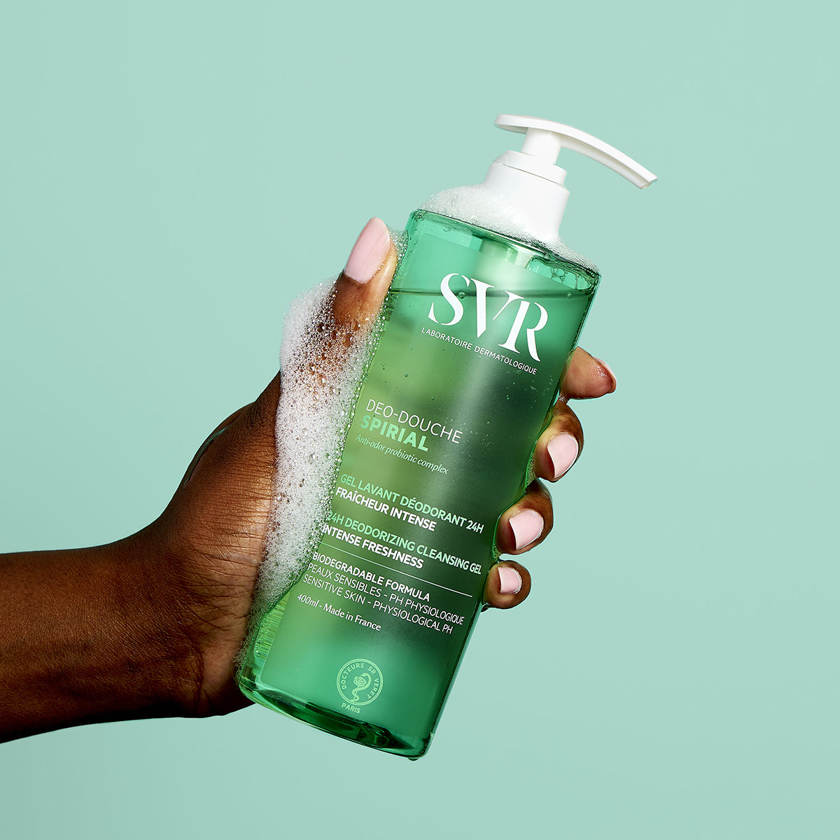 Recipient transparent de 400ml cu gel de duș SVR Spirial, ținut în mână, cu text alb și pompă albă pe fundal verde mentă.
