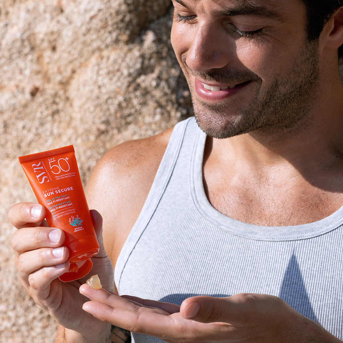 Bărbat aplicând gelul solar transparent SVR Sun Secure Extrême SPF50+ dintr-un tub portocaliu, pe fundal stâncos.