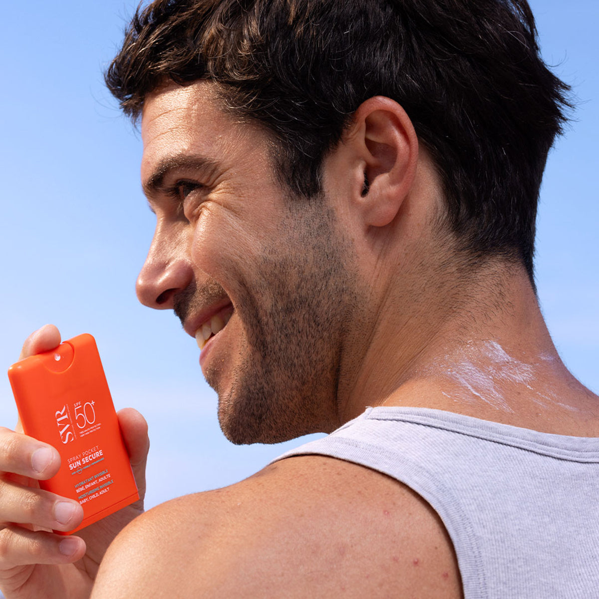 Bărbat aplicând spray solar portabil SVR Sun Secure SPF50+ pe piele, într-un recipient portocaliu compact.