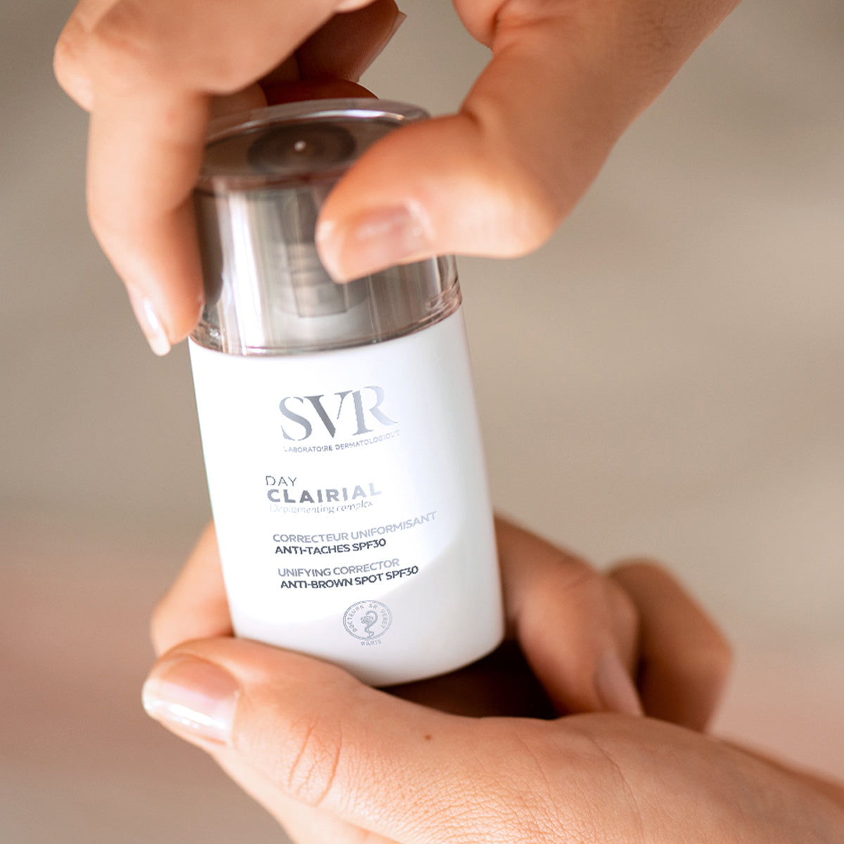 Mâini care deschid flaconul alb SVR Clairial Day, corector anti-pete cu SPF30, design minimalist și capac transparent.
