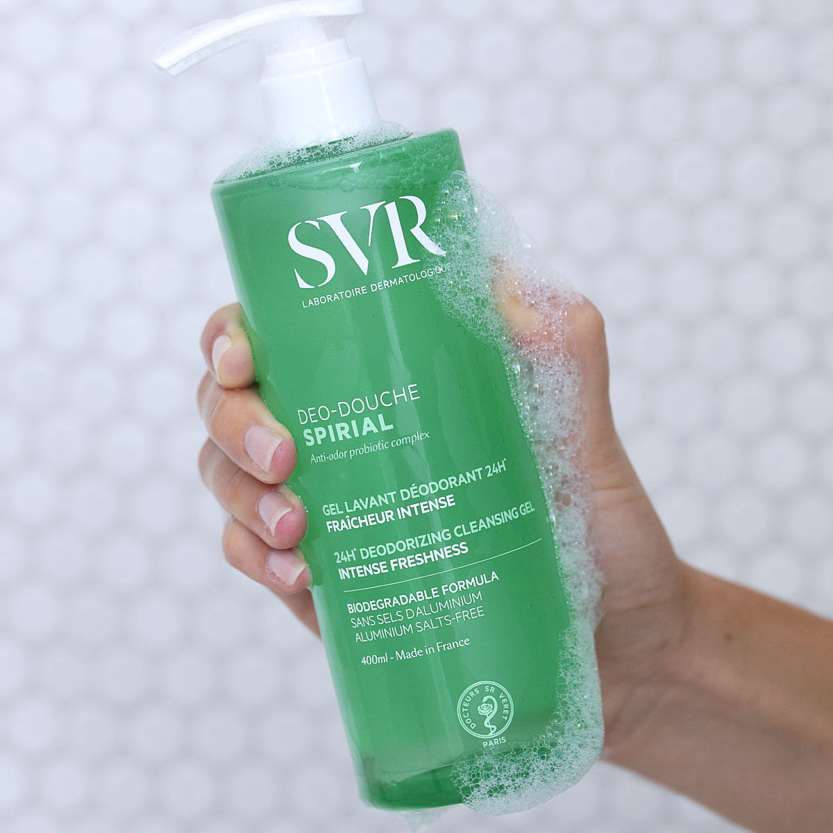 Recipient verde de 400 ml SVR Spirial Déo-Douche cu pompiță, ținut în mână și acoperit cu spumă de curățare.