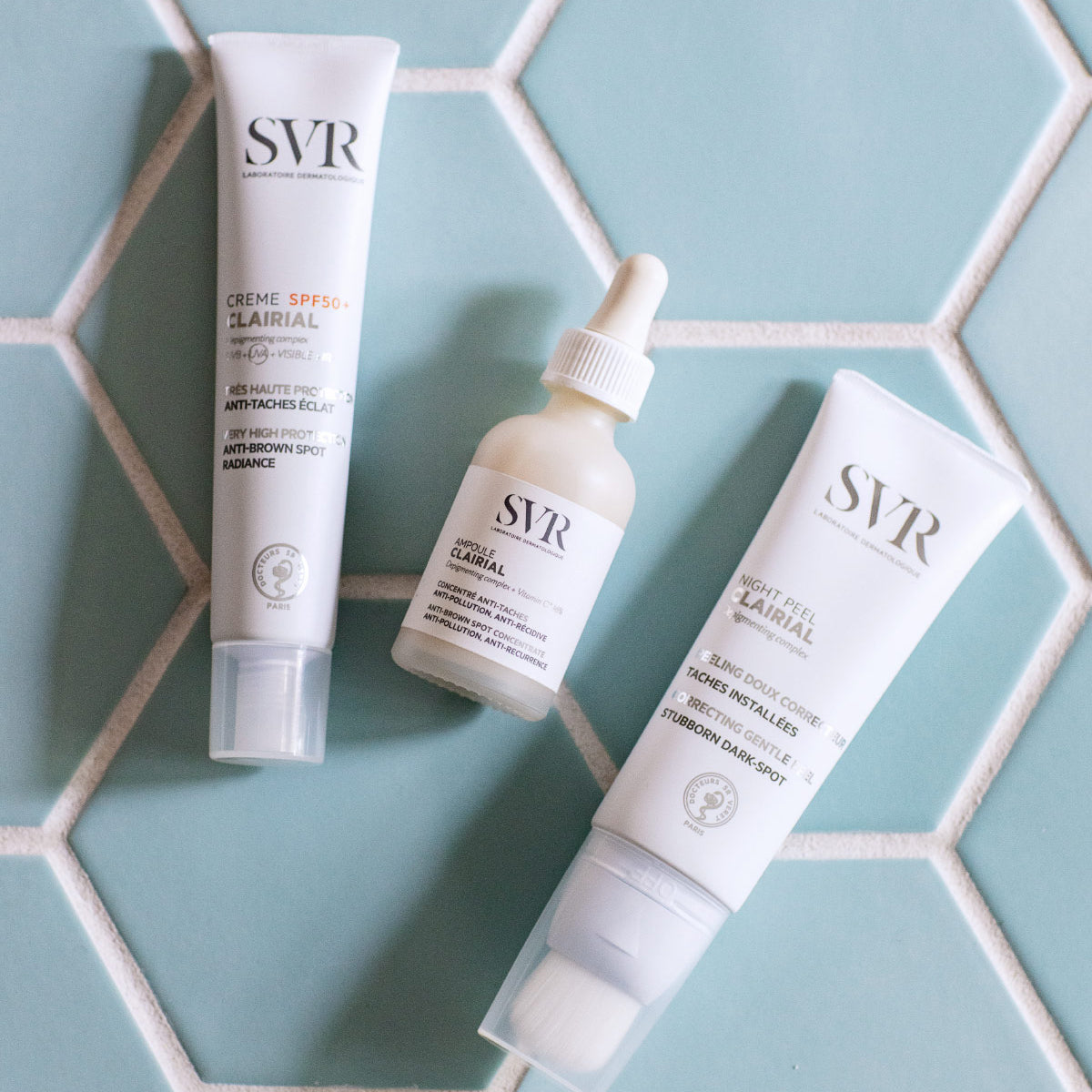 Produse SVR Clairial: cremă SPF, ser și Night Peel cu aplicator, dispuse pe un fundal de faianță albastră hexagonală.