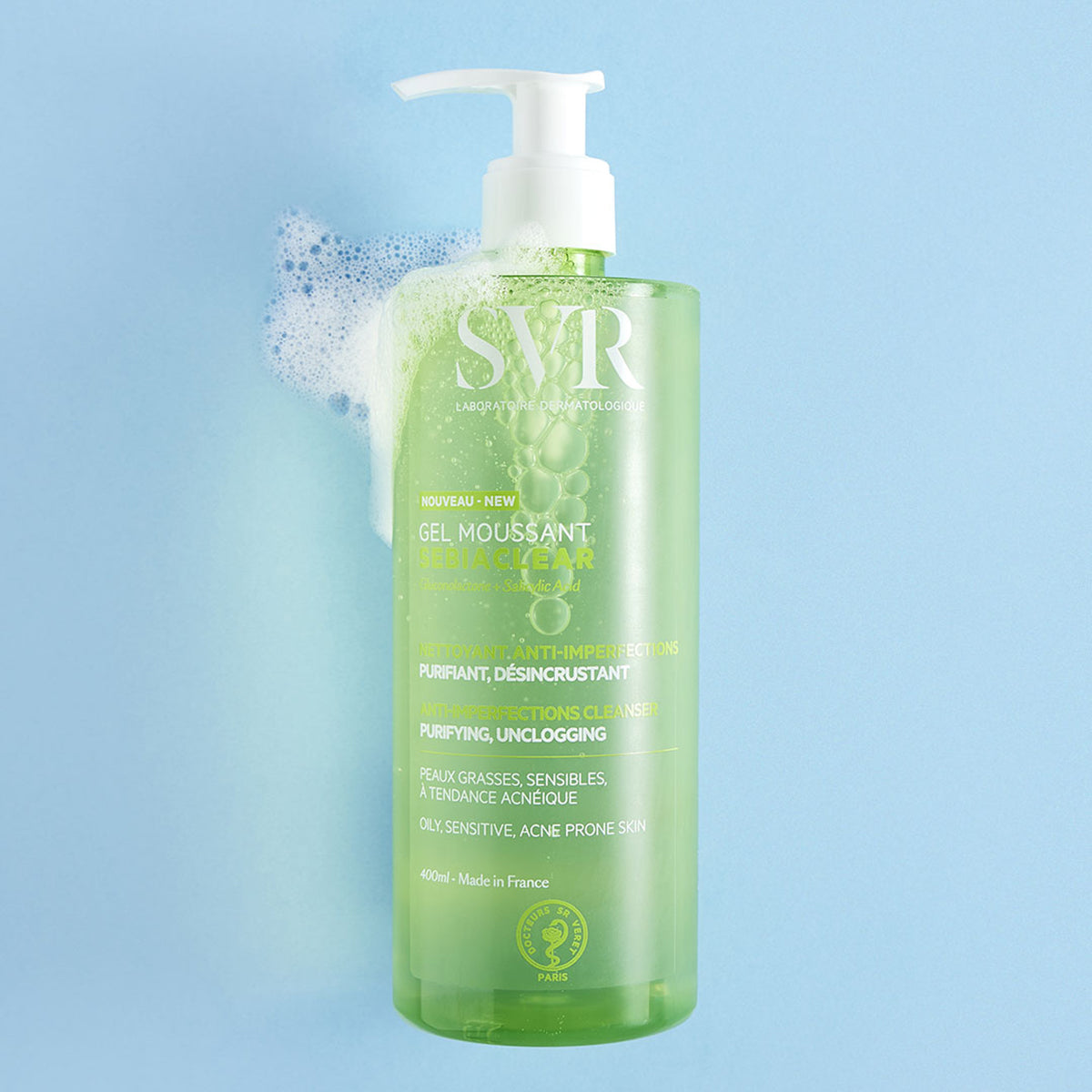 Recipient transparent de 400ml cu gel de curățare verde SVR Sebiaclear, pompă albă și spumă pe fundal albastru deschis.