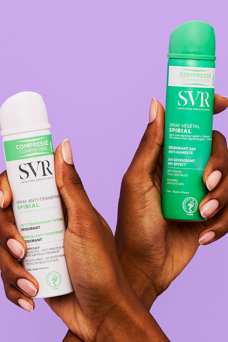 Two hands holding white and green SVR Spirial deodorant spray cans against a purple background.