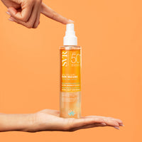 Spray SVR SUN SECURE Eau Solaire SPF50+ într-un flacon transparent cu textură bifazică, susținut între mâini pe fundal portocaliu.