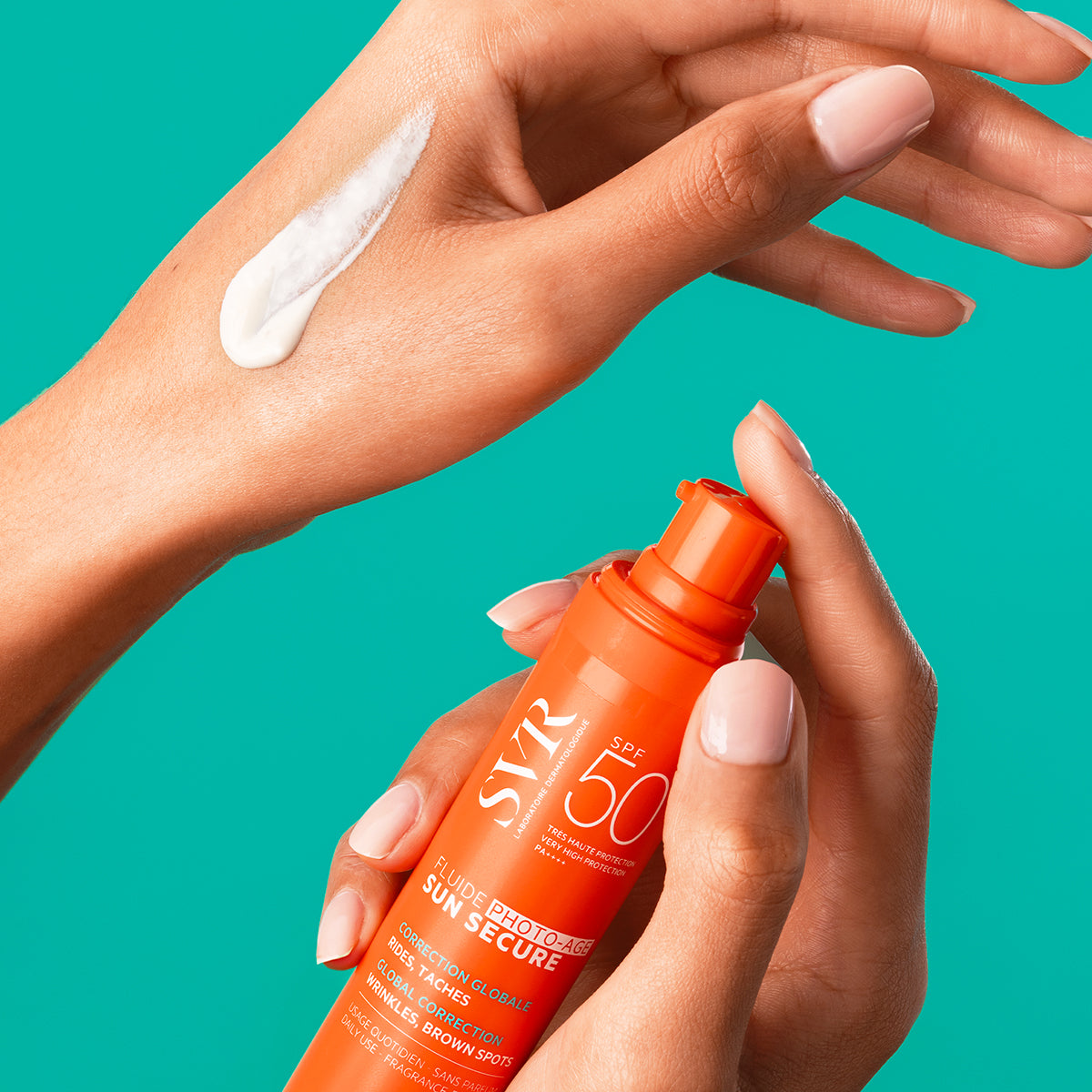 Hands holding an orange SVR SUN SECURE SPF50+ pump bottle with white sunscreen cream swiped on the skin against a teal background.