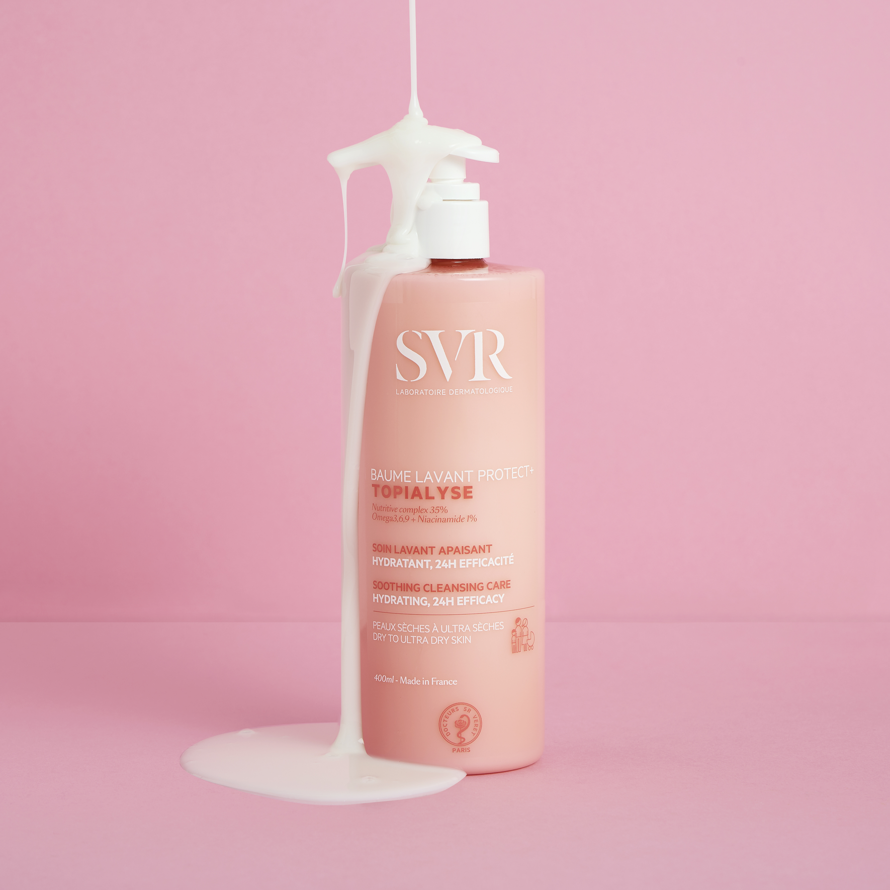Recipient SVR Topialyse Baume Lavant de 400 ml cu textură cremoasă care curge pe fundal roz, ideal pentru pielea uscată.