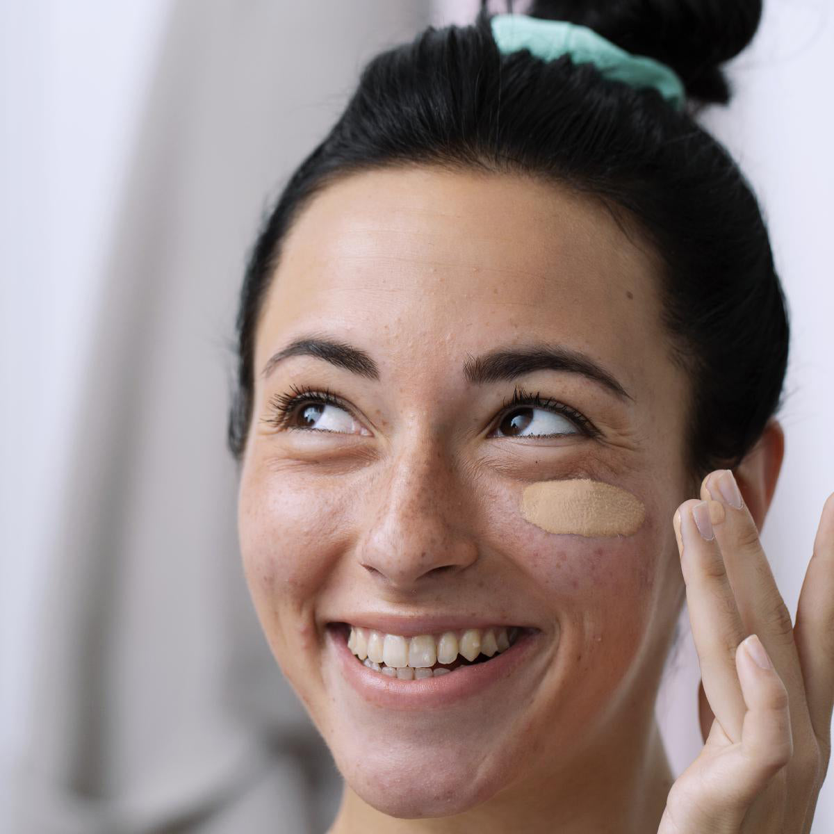 Femeie zâmbitoare aplicând cremă nuanțatoare SVR Sebiaclear pe obraz pentru a acoperi imperfecțiunile tenului acneic.