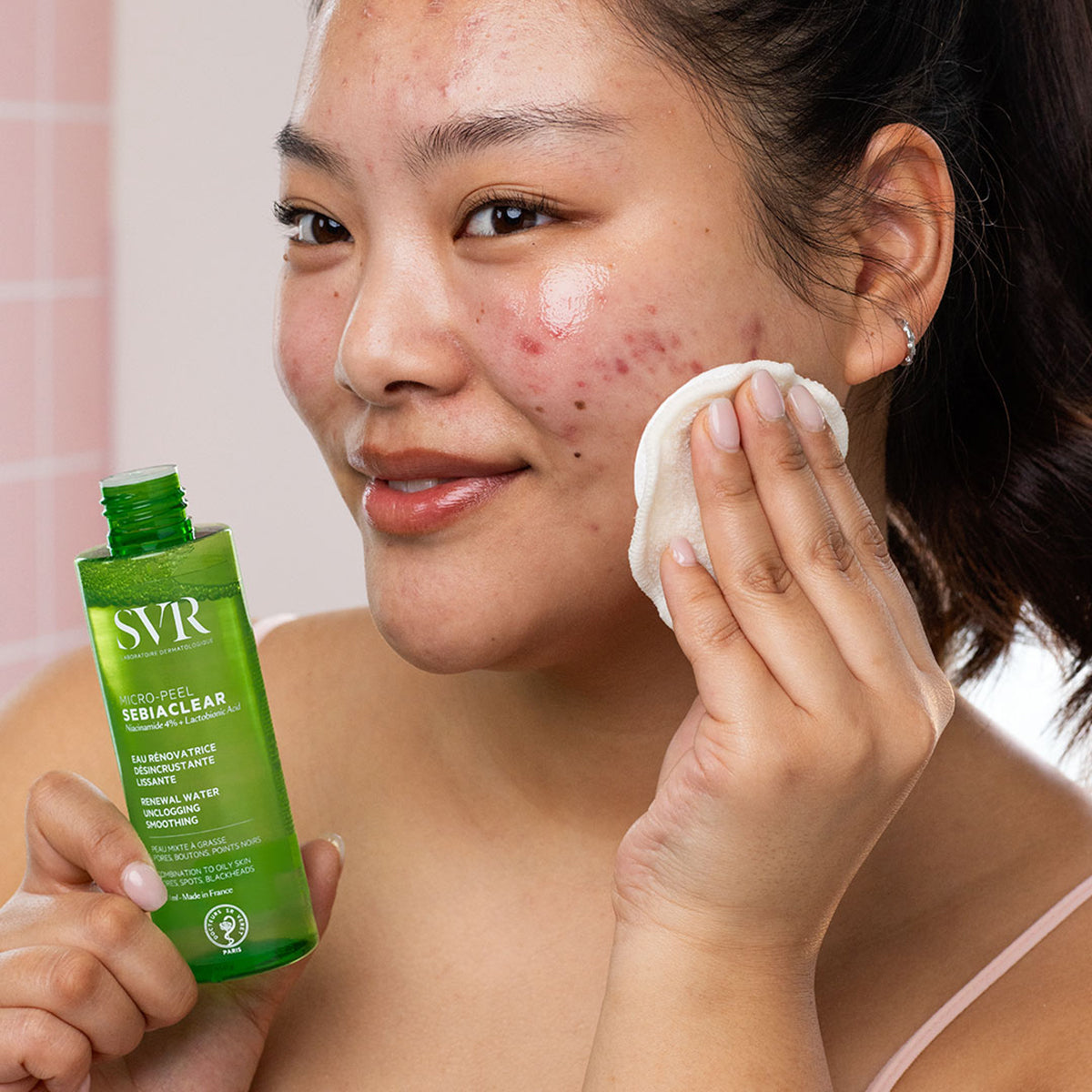 Femeie aplicând loțiunea SVR Sebiaclear Micro-Peel cu o dischetă demachiantă pe tenul cu imperfecțiuni.