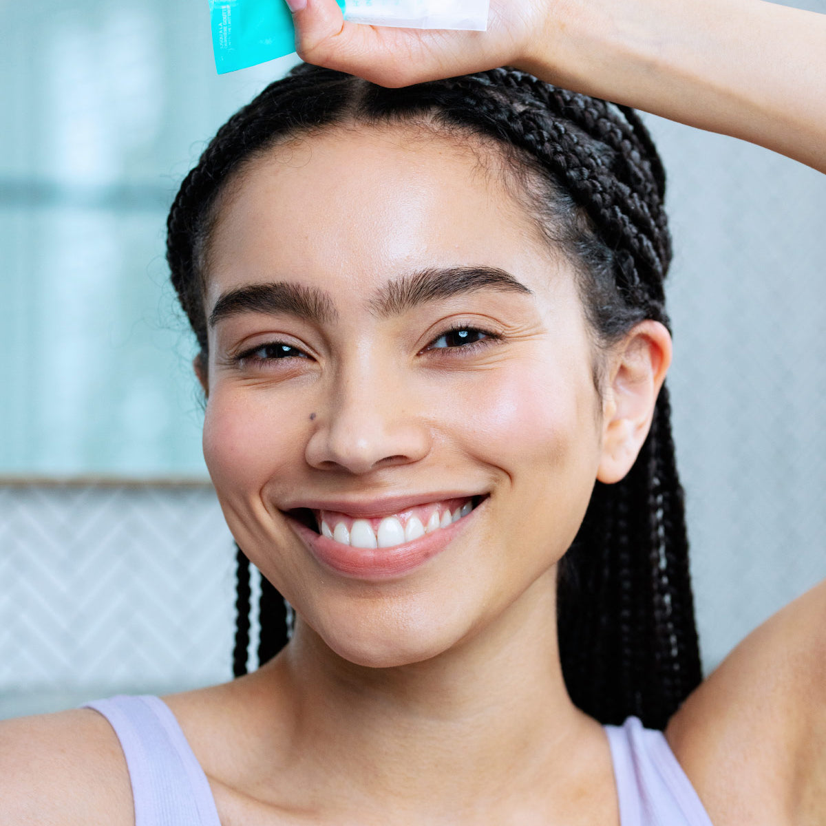 Femeie zâmbitoare ținând deasupra capului ambalajul eco-friendly Hydraliane Crème de culoare albastru-turcoaz.