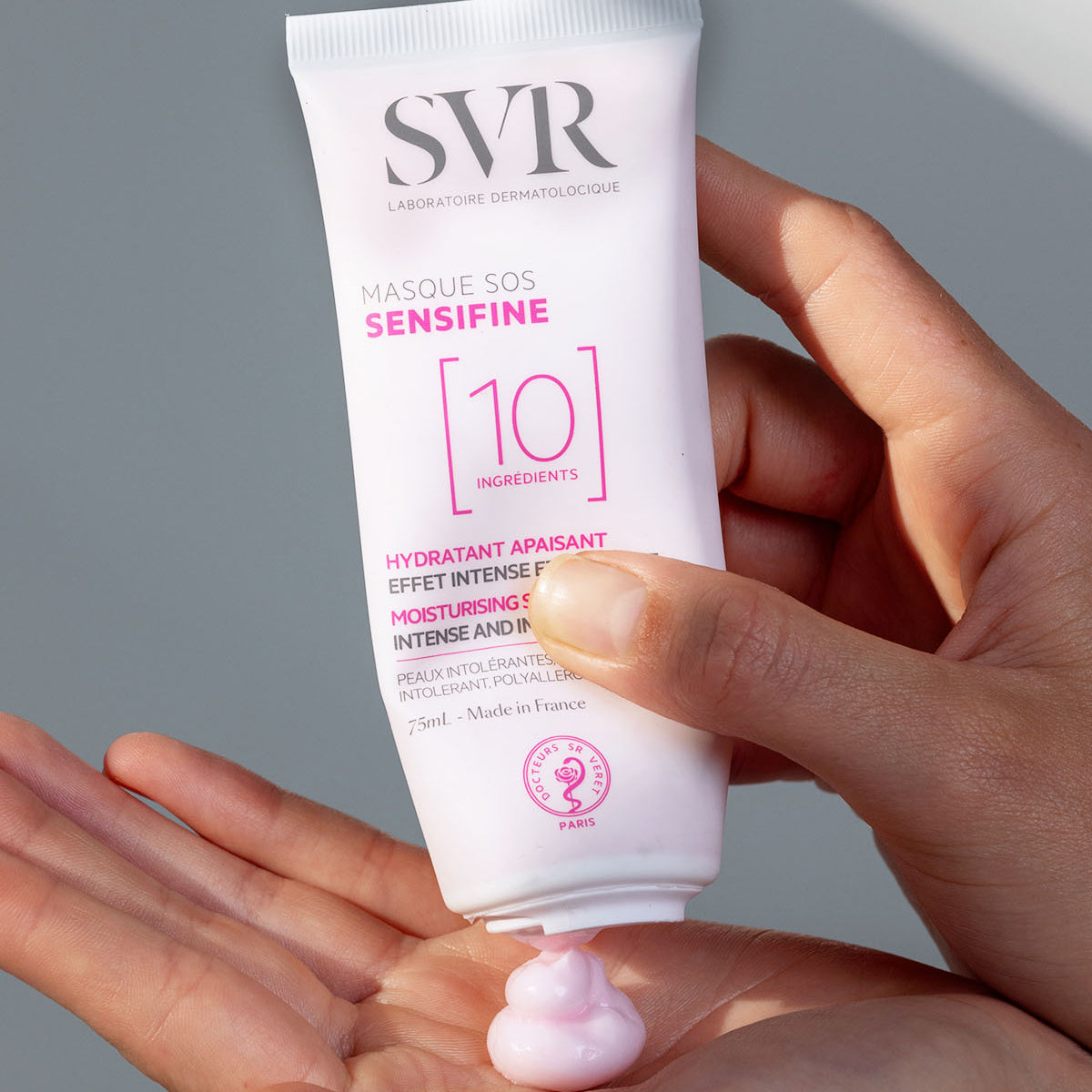 SVR Sensifine Masque SOS white 75ml tube dispensing a dollop of pale pink cream into a hand.