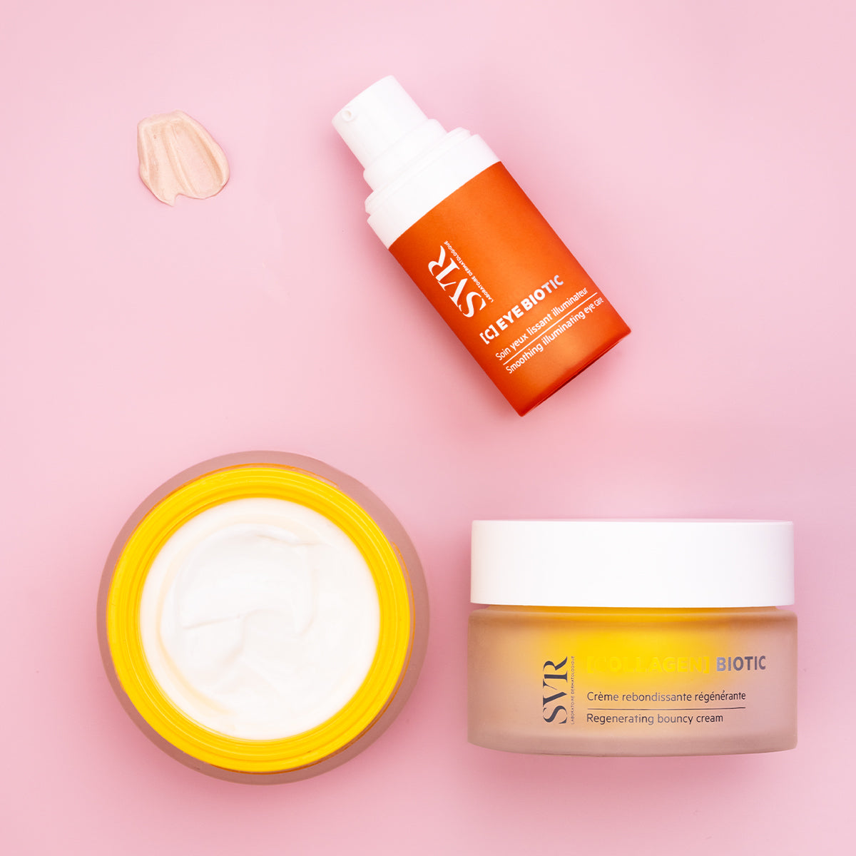 SVR C-EYE BIOTIC pump bottle and Collagen Biotic cream jar with white lids on a pink background with a cream swatch.