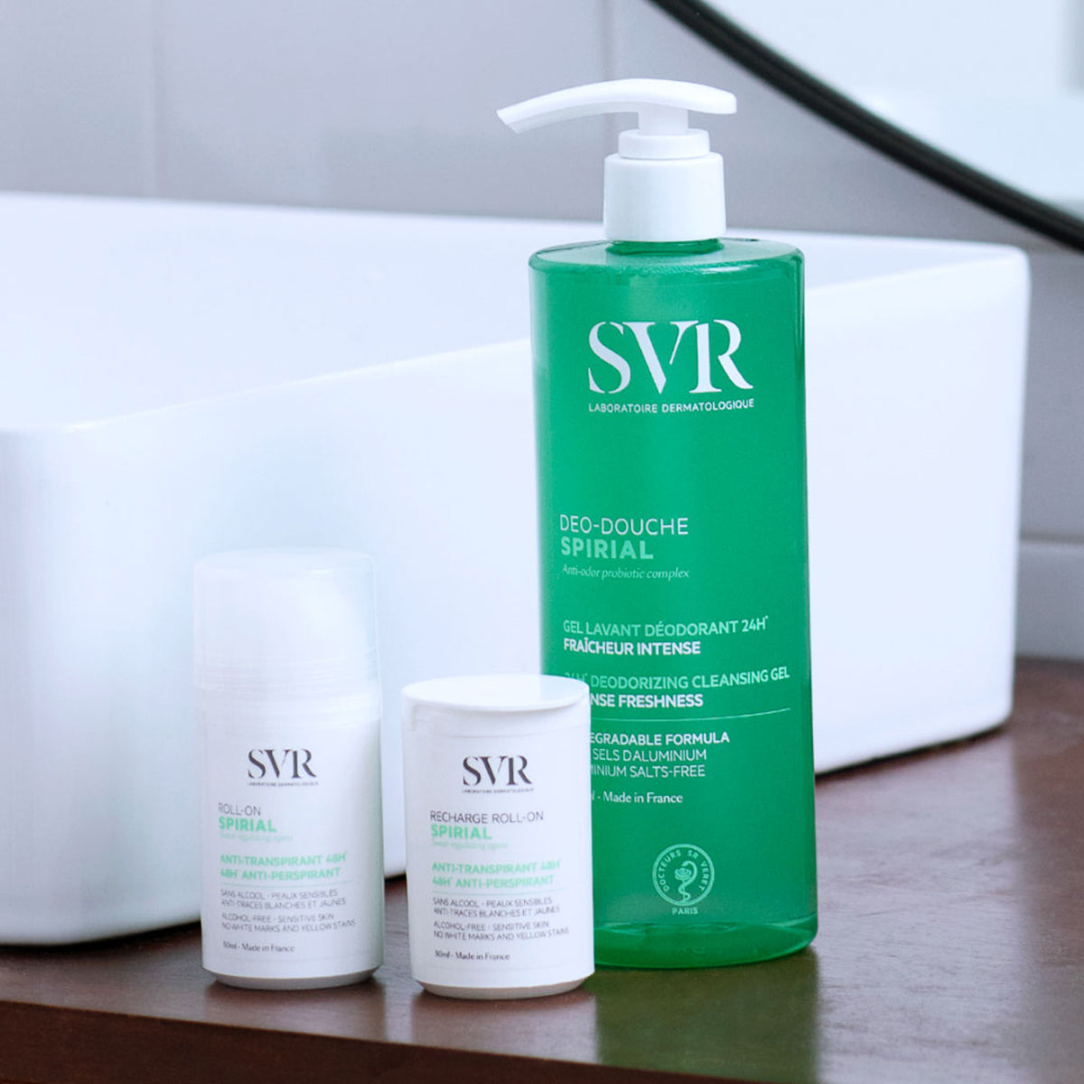 Produse SVR Spirial: roll-on alb, rezervă și gel de duș deodorant verde, așezate pe un blat lângă o chiuvetă albă.