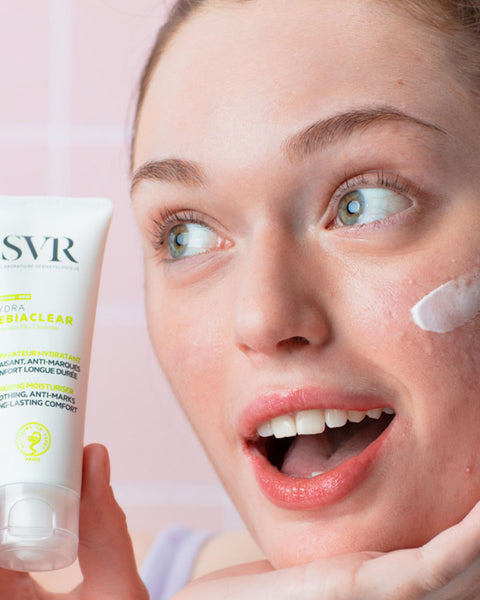 Woman holding SVR Sebiaclear Hydra moisturizer tube with cream on her cheek.