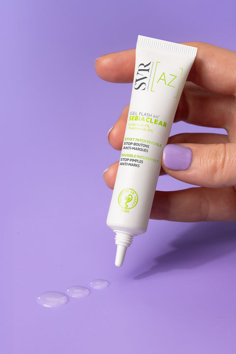 Hand holding a white SVR Sebiaclear AZ gel tube over a purple surface with three small drops of clear gel.