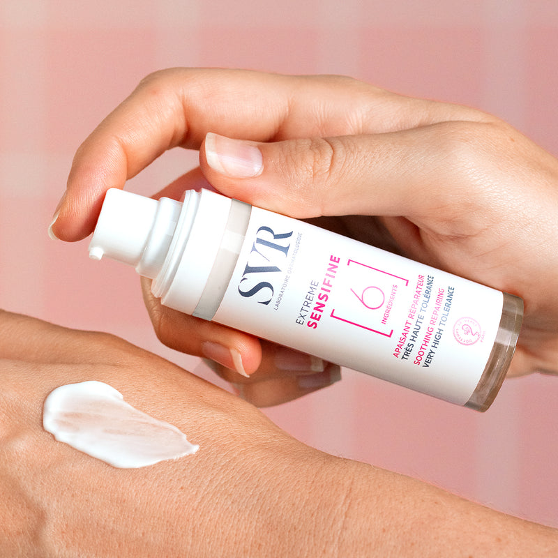 Hand applying SVR Sensifine Extreme soothing repair cream from a white pump bottle onto skin.