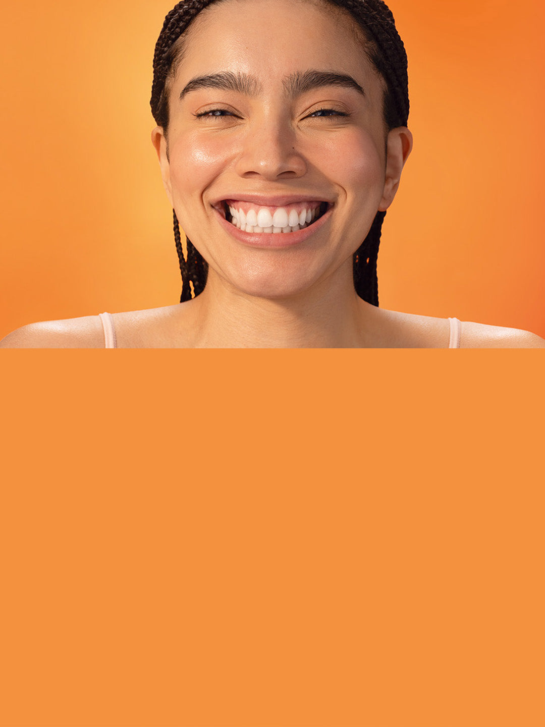 Smiling woman with braided hair and glowing skin against a vibrant orange background.